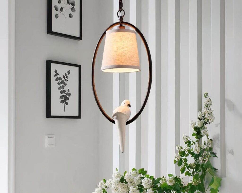 Suspension cage oiseau élégante style champêtre avec des tableaux à gauche, un rideau en fond et une plante verte en bas.