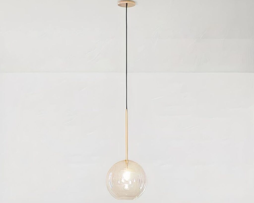 Suspension globe au design moderne et épuré en verre allumée sur fond gris.