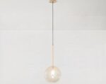 Suspension globe au design moderne et épuré en verre allumée sur fond gris.