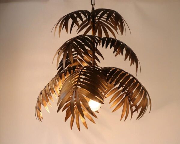 Suspension jungle palmier doré, l'ampoule est allumée et la suspension est accrochée. Fond beige.