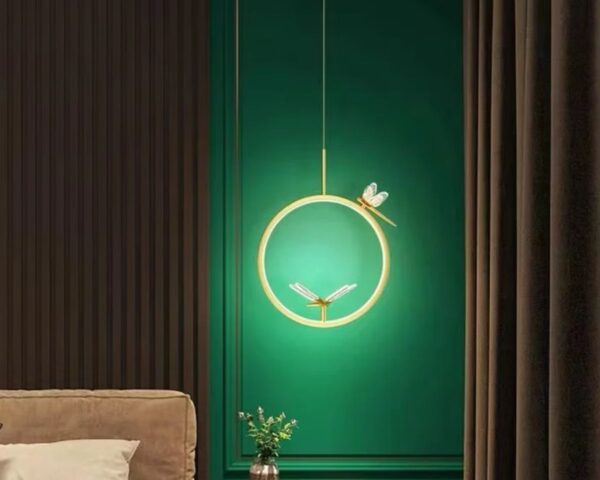 Suspension libellule cercle enchanté, de couleur dorée, suspendue et allumée. Elle se situe dans une pièce de vie type salon.