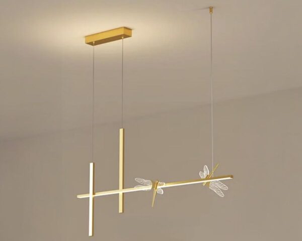 Suspension libellule éclat doré, avec deux libellules, le tout de couleur dorée, luminaire suspendu et allumé. Fond beige.