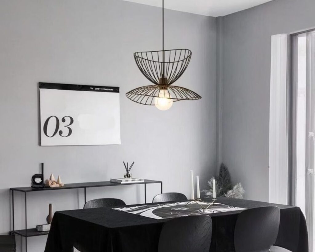 Suspension libellule fleur lumineuse, de couleur noire, suspendue et allumée au-dessu d'une table noire rectangulaire. Le mur de derrière est gris avec un affichage blanc.