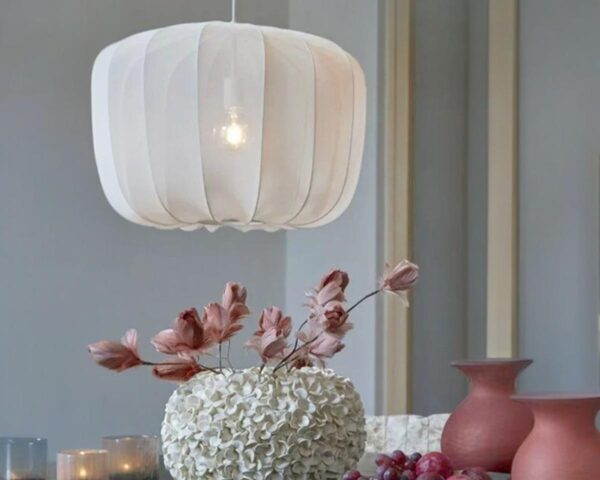 Suspension lin design épuré, de couleur blanche, suspendue et allumée au-dessus d'un vase avec des fleurs dedans.