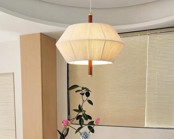 Suspension lin silhouette contemporaine allumée au-dessus d'une table. En arrière-plan, une fenêtre avec des persiennes.