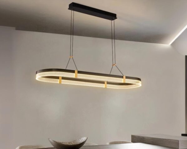 Suspension métal ovale et moderne allumée au-dessus d'une table rectangulaire en bois.