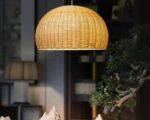 Suspension osier demi sphère, allumée, suspendue au-dessus d'une table en bois dans un décor cosy.