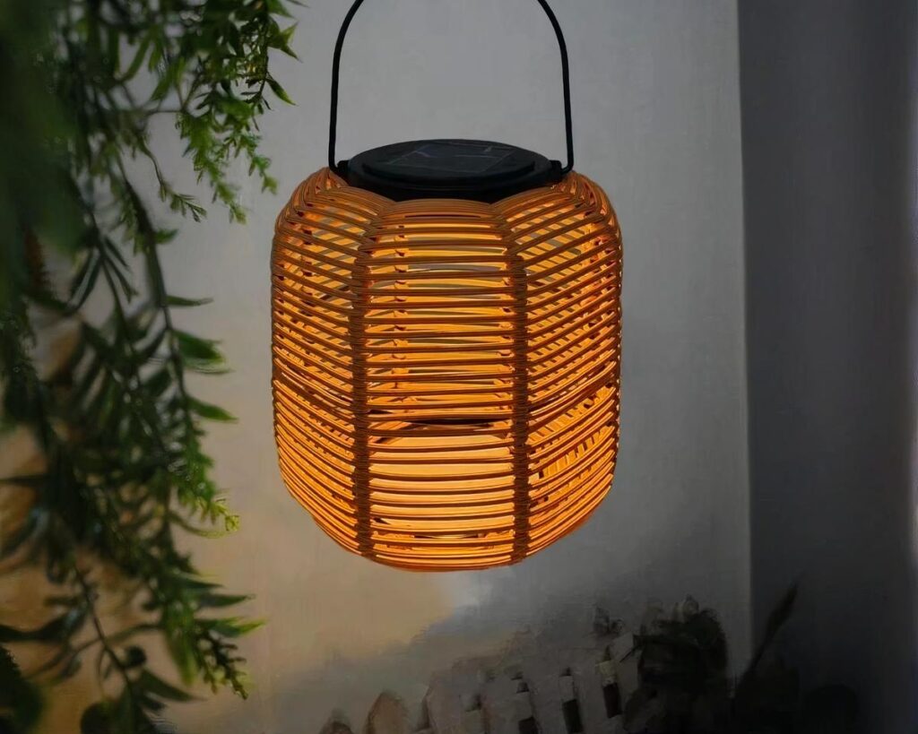 Suspension solaire lanterne effet rotin, allumée et accrochée à côté d'une plante verte.