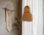Suspension style raphia en cloche frangée, installé dans une pièce de vie à côté d'une grande fenêtre avec des rideaux blanc.