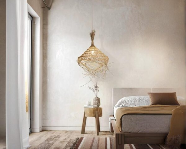 Suspension style raphia LED effet chapeau, installée au-dessus d'une table de nuit à côté d'un lit. Le mur derrière est gris clair.