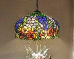 Suspension style Tiffany multicolore fleurie, avec une ampoule allumée, au-dessus d'un bouquet de fleur.