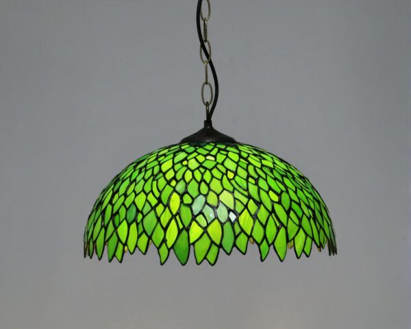Suspension style Tiffany verte, avec une ampoule allumée, un fond gris derrière.