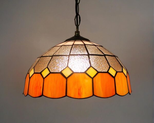 Suspension style Tiffany vintage orange et transparente avec une ampoule allumée.