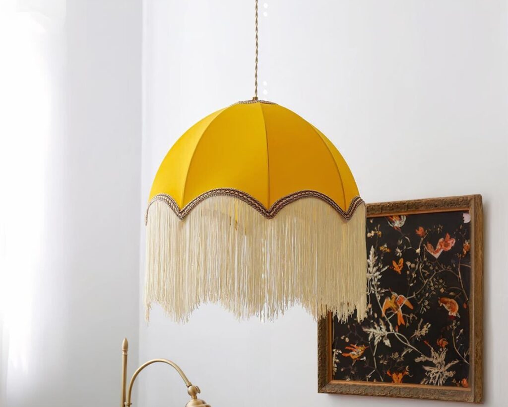 Suspension tissu LED tendance avec frange avec un tableau sur un mur gris en fond.