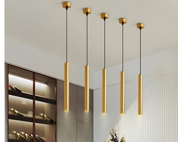 Suspension tube dorée design et créative allumée dans une salle à manger avec une étagère intégrée contenant des bouteilles de vins.