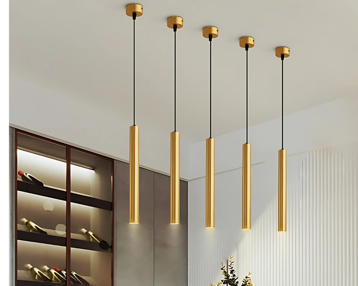 Suspension tube dorée design et créative allumée dans une salle à manger avec une étagère intégrée contenant des bouteilles de vins.