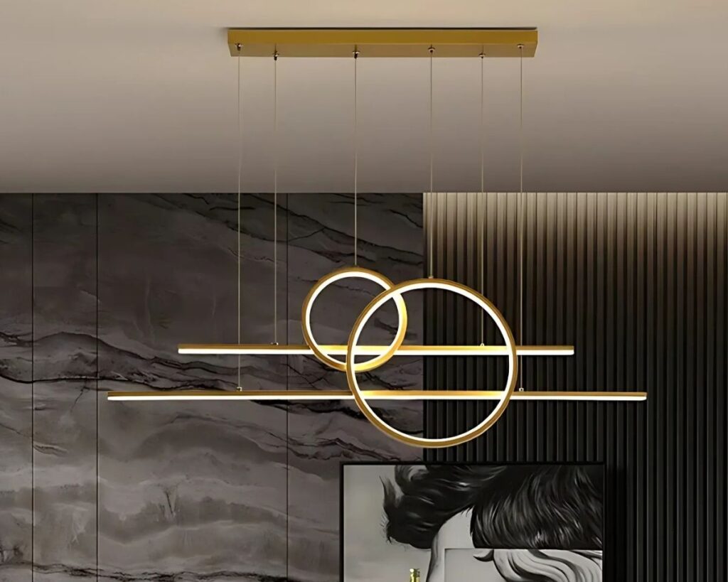 Suspension XXL art moderne dorée, avec deux cercles et deux barres latéral, allumée, suspendue au-dessus d'une table et dans un décor de salon.