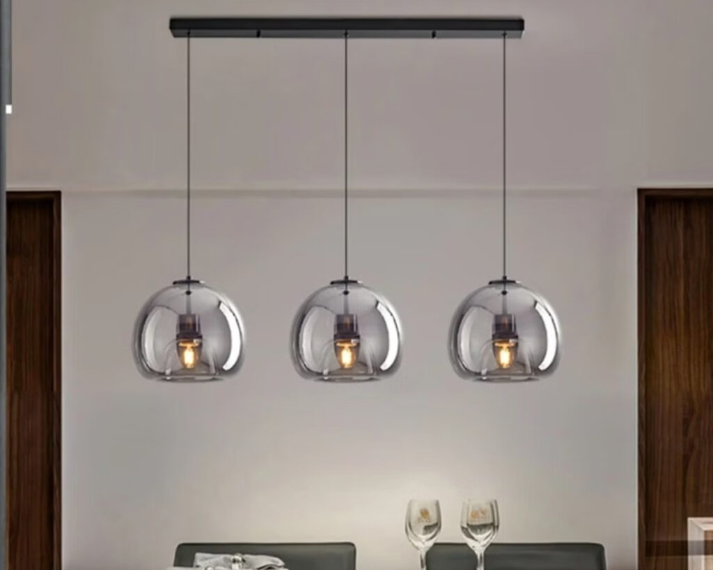 Suspension couloir à trois têtes en verre fumé tenu sur une barre noire au plafond. Au-dessus s'une taable avec deux verres à pied posés dessus. Le mur est beige.