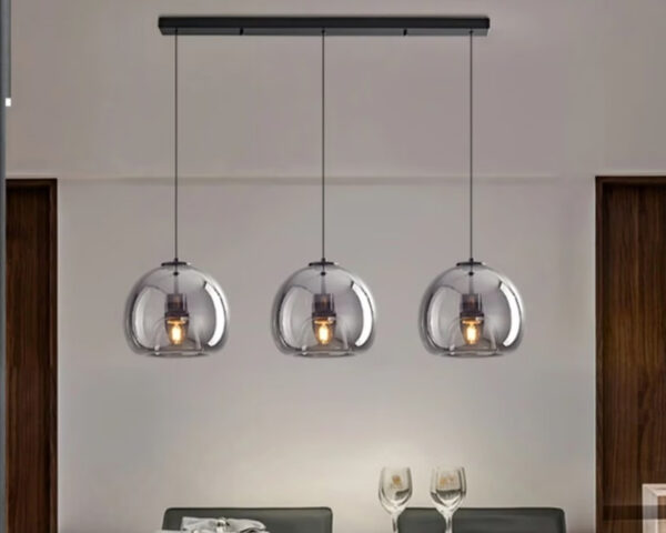 Suspension couloir à trois têtes en verre fumé tenu sur une barre noire au plafond. Au-dessus s'une taable avec deux verres à pied posés dessus. Le mur est beige.