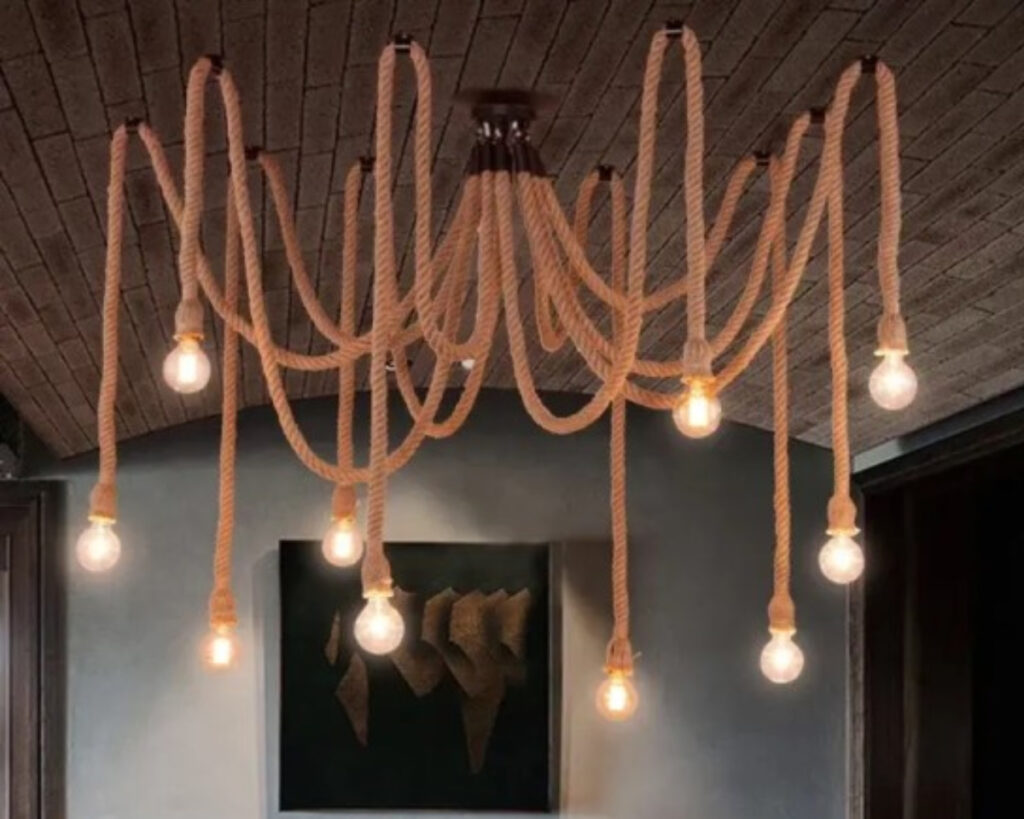 Suspension araignée vintage au design innovant formée de plusieurs cordes avec des ampoules à leurs extrémités. Chaque ampoule est allumée. Dans une pièce au mur blanc et au plafond marron.