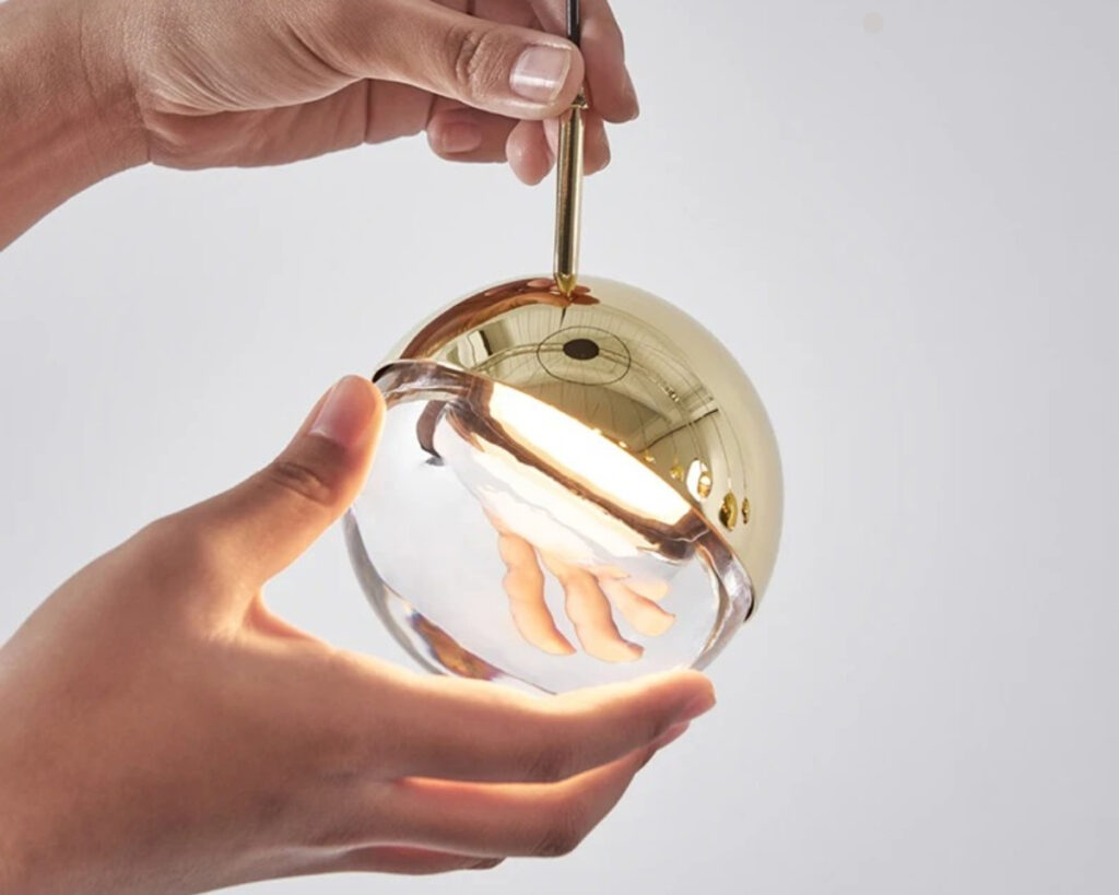 Suspension ampoule élégante au style moderne dorée sur fond gris tenue dans une main