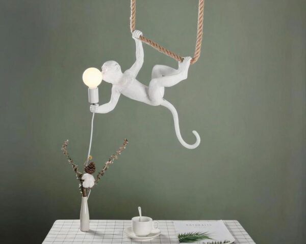 Suspension singe acrobate accroché à une corde, au-dessus d'une table carrée. Avec un mur kaki au fond.
