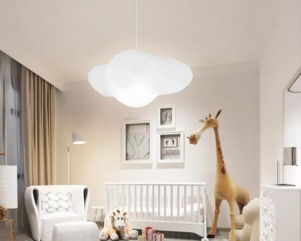 Suspension nuage blanche et minimaliste dans une chambre de bébé avec un lit blanc à barreaux, un fauteuil blanc à sa gauche et une grande girafe à droite.
