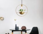 Suspension cuivre dorée et moderne pour plante. Fixée au-dessus d'une table noire ronde avec une chaise à sa droite.