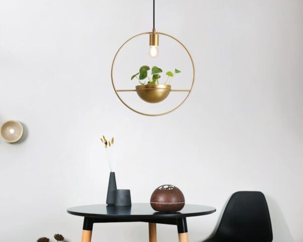 Suspension cuivre dorée et moderne pour plante. Fixée au-dessus d'une table noire ronde avec une chaise à sa droite.