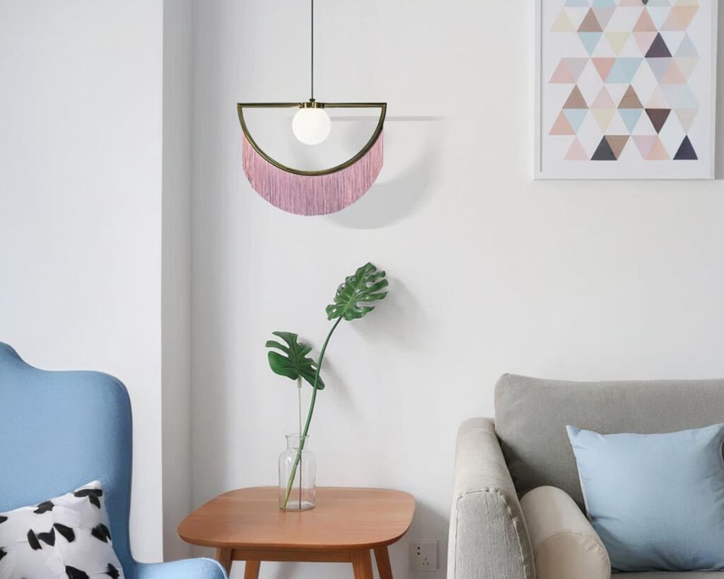 Suspension tissu rose et dorée au design moderne dans un salon avec un canapé gris sur la droite et un fauteuil bleu à gauche.