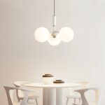 Suspension boule en verre chic, de couleur blanche, allumée et suspendue au-dessus d'une table de salle à manger. Fond beige clair.