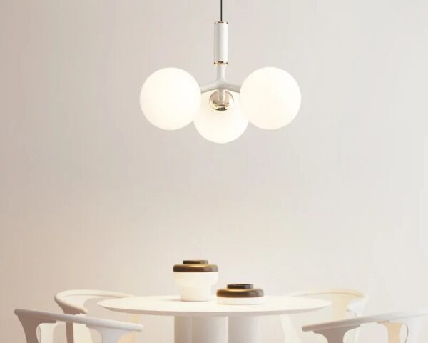 Suspension boule en verre chic, de couleur blanche, allumée et suspendue au-dessus d'une table de salle à manger. Fond beige clair.