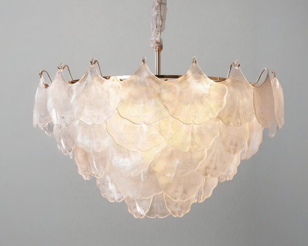 Suspension coquillage en cristal en forme de triangle pointe vers le bas. L'ampoule est allumée. Sur fond gris.
