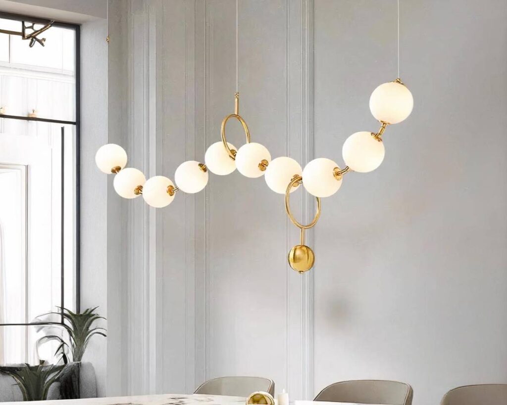 Suspension multiple LED dorée et artistique installée au-dessus d'une table avec des chaises et une fenêtre et une plante à gauche