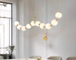 Suspension multiple LED dorée et artistique installée au-dessus d'une table avec des chaises et une fenêtre et une plante à gauche