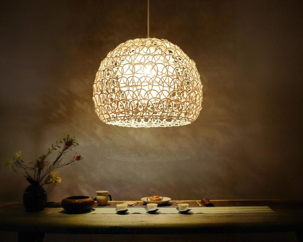Suspension naturelle avec abat-jour ajouré, allumée et suspendue au-dessus d'une table avec un fond sombre.