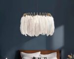 Suspension plume dorée et décorative allumée dans une chambre aux murs bleu canard avec un lit deux places marron et deux coussins blancs.