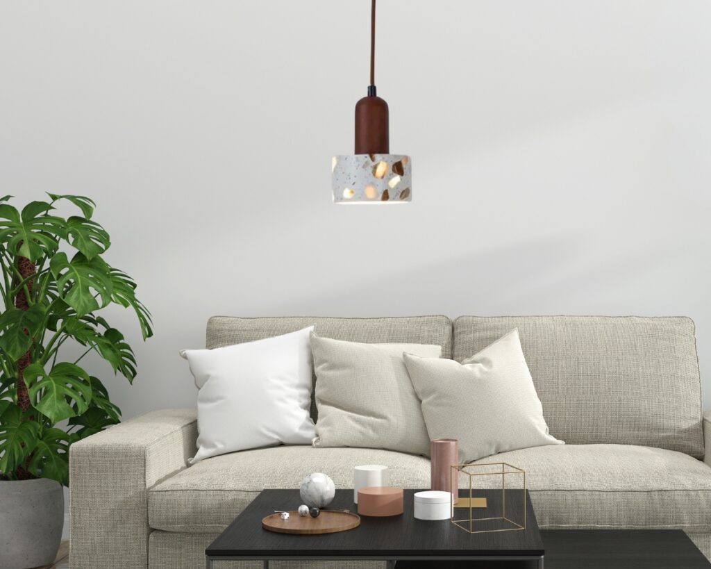 Suspension terre cuite de style terrazzo dans un salon au-dessus d'une table basse noire. Un canapé beige contre le mur blanc et une plante verte à sa gauche.