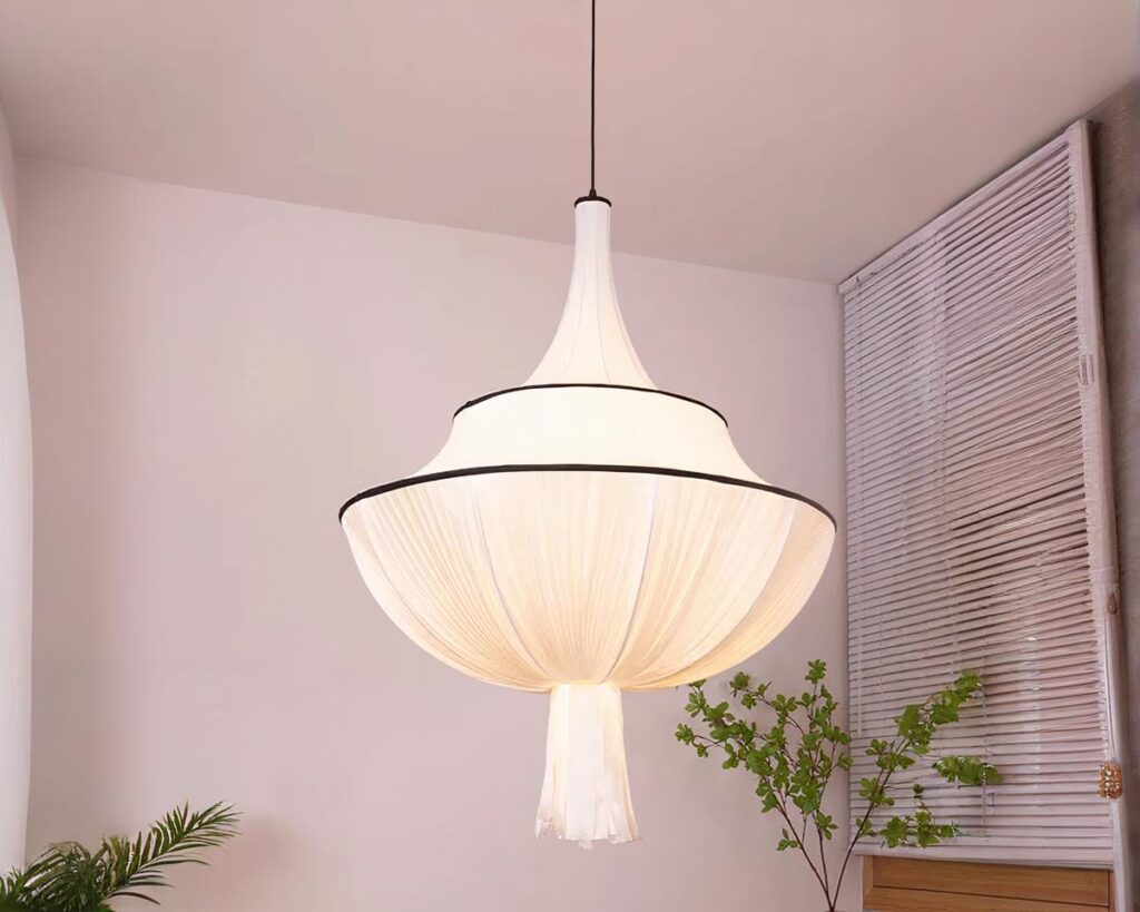 Suspension tissu drapé blanc, allumée et suspendue. Une plante verte est derrière et un fond beige clair.