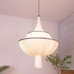 Suspension tissu drapé blanc, allumée et suspendue. Une plante verte est derrière et un fond beige clair.