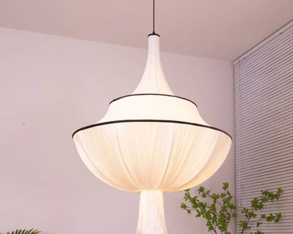 Suspension tissu drapé blanc, allumée et suspendue. Une plante verte est derrière et un fond beige clair.