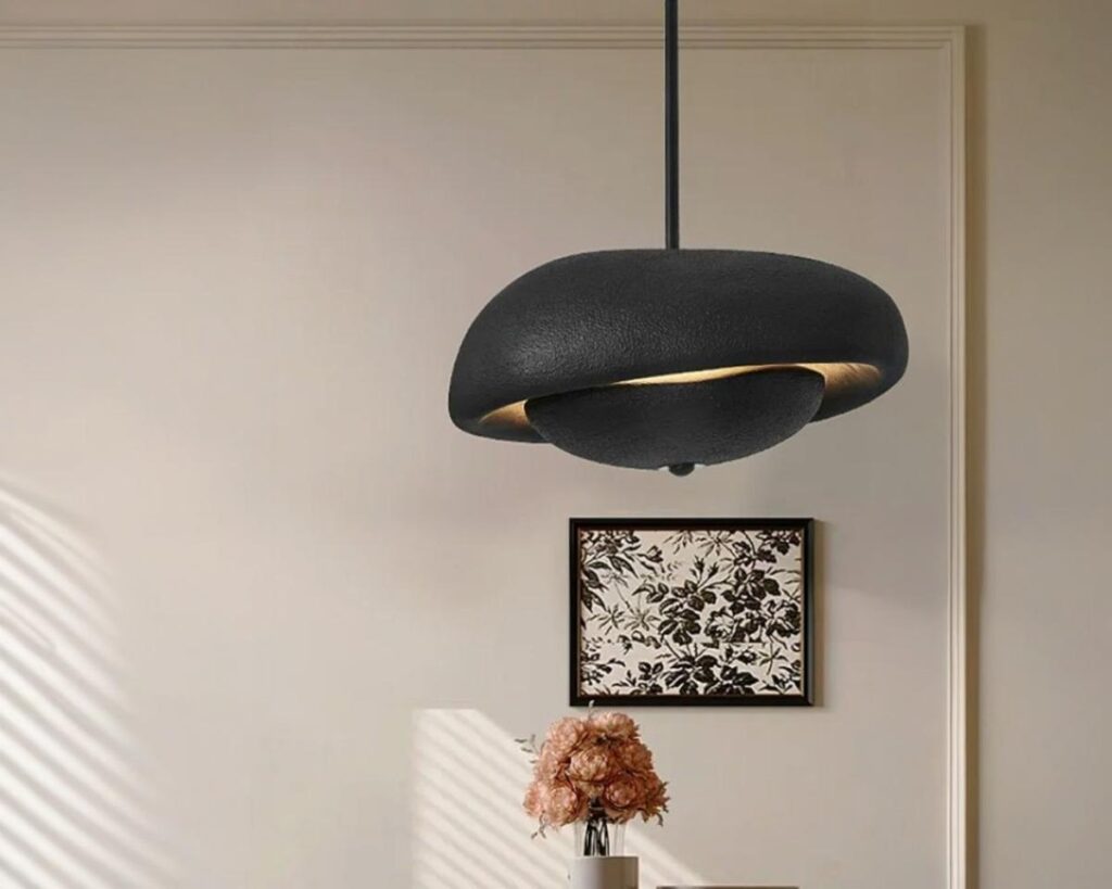 Suspension LED en forme de galet, de couleur noire, suspendue et allumée au-dessus d'une table. Fond beige.