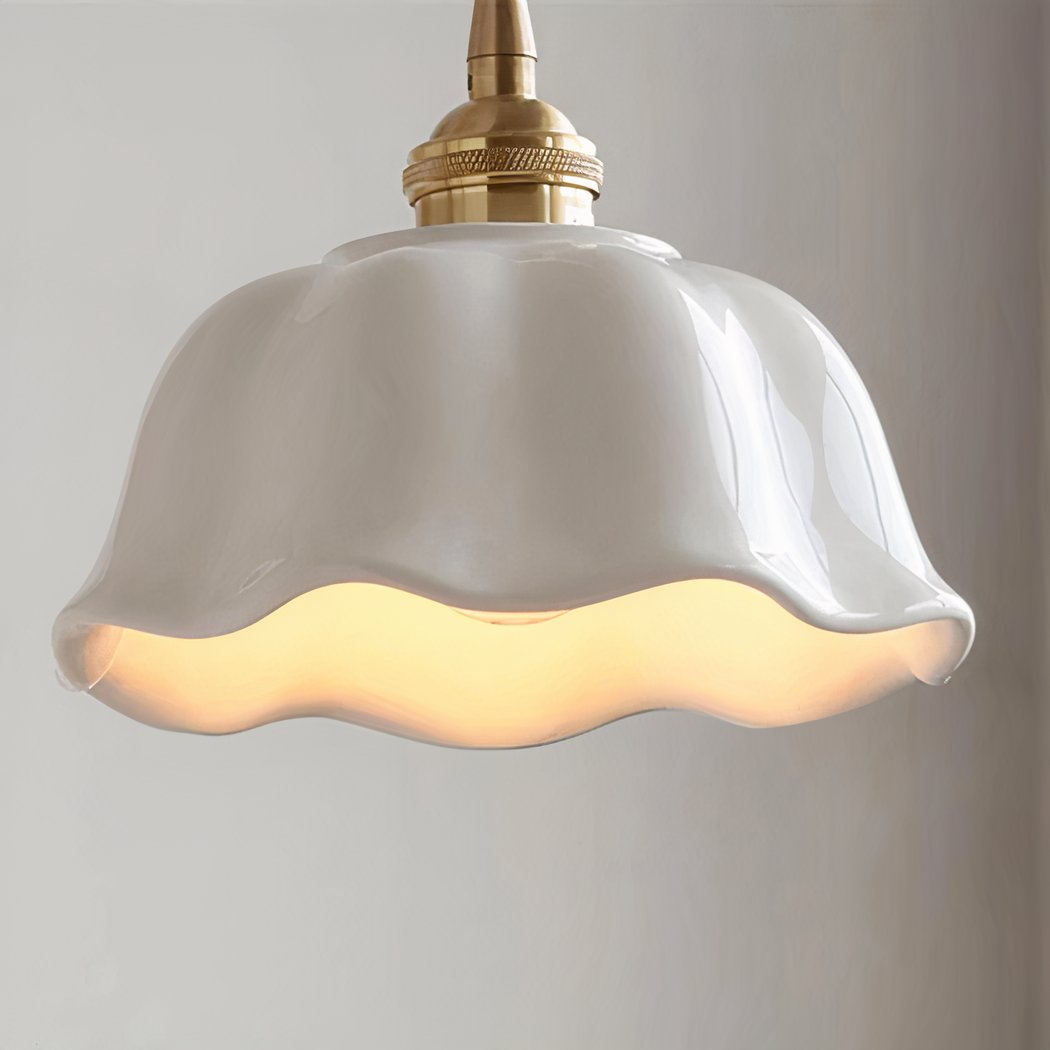 Une suspension en céramique blanche à bord ondulé campagne chic, avec abat-jour blanc brillant et lumière chaude, suspendue devant un mur clair.