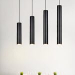 Quatre suspensions tube noire design minimaliste pendent au plafond dans une pièce claire et épurée.