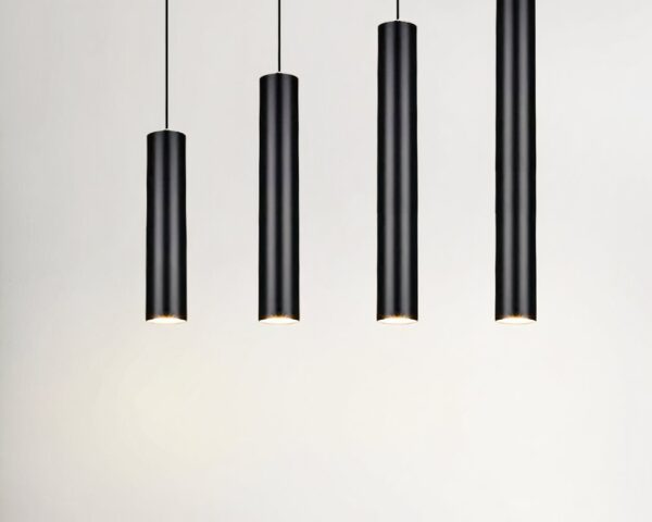 Quatre suspensions tube noire design minimaliste pendent au plafond dans une pièce claire et épurée.