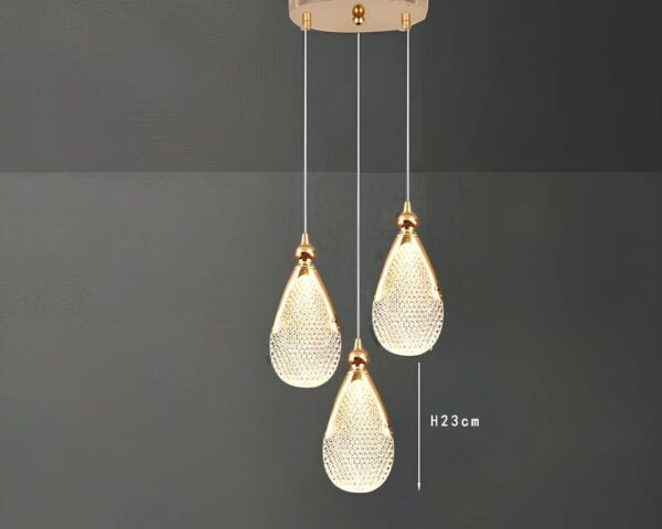 Une suspension goutte d’eau en acrylique doré avec un abat-jour en forme de goutte brillante, suspendue à un long fil sur fond gris.