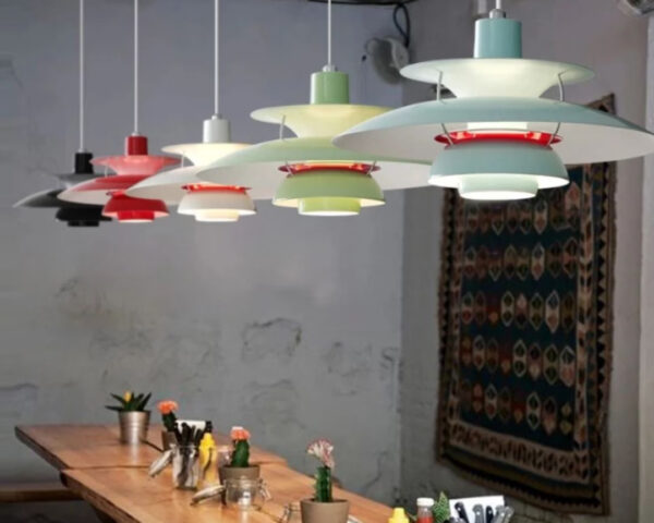 Une suspension design danois à abat-jour multicouches colorée, suspendue au-dessus d’une table en bois dans une salle à manger simple et lumineuse.