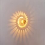 Une applique murale LED à effet halo lumineux circulaire diffuse une lumière jaune douce sur un mur clair, avec un joli motif en forme de soleil autour.